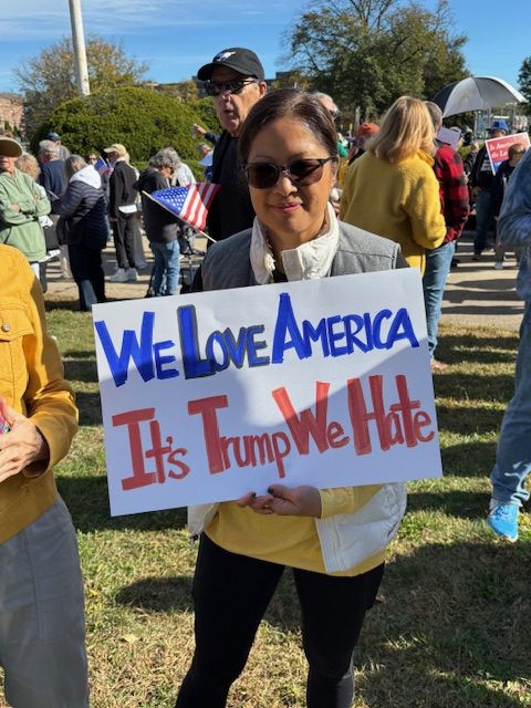 A woman holds a handmade sign that says, "We Love America. It's Trump We Hate."